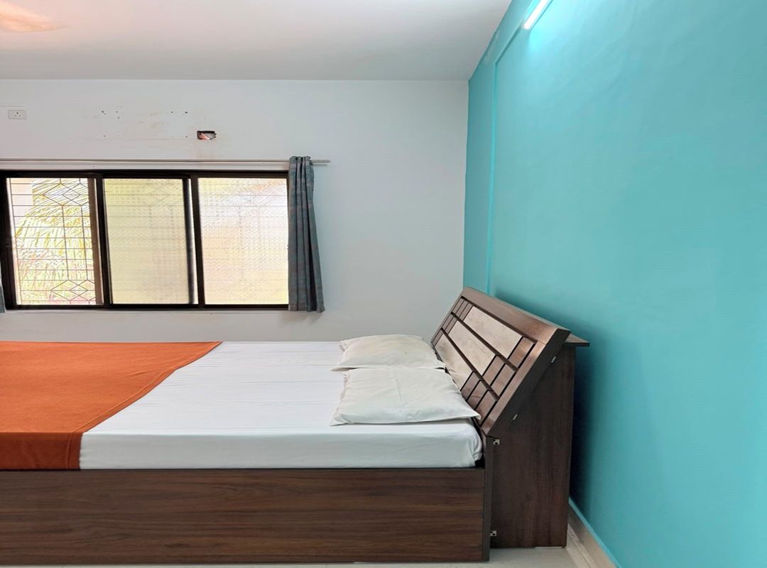 A bedroom with a bed, a window with curtains, and a teal wall.