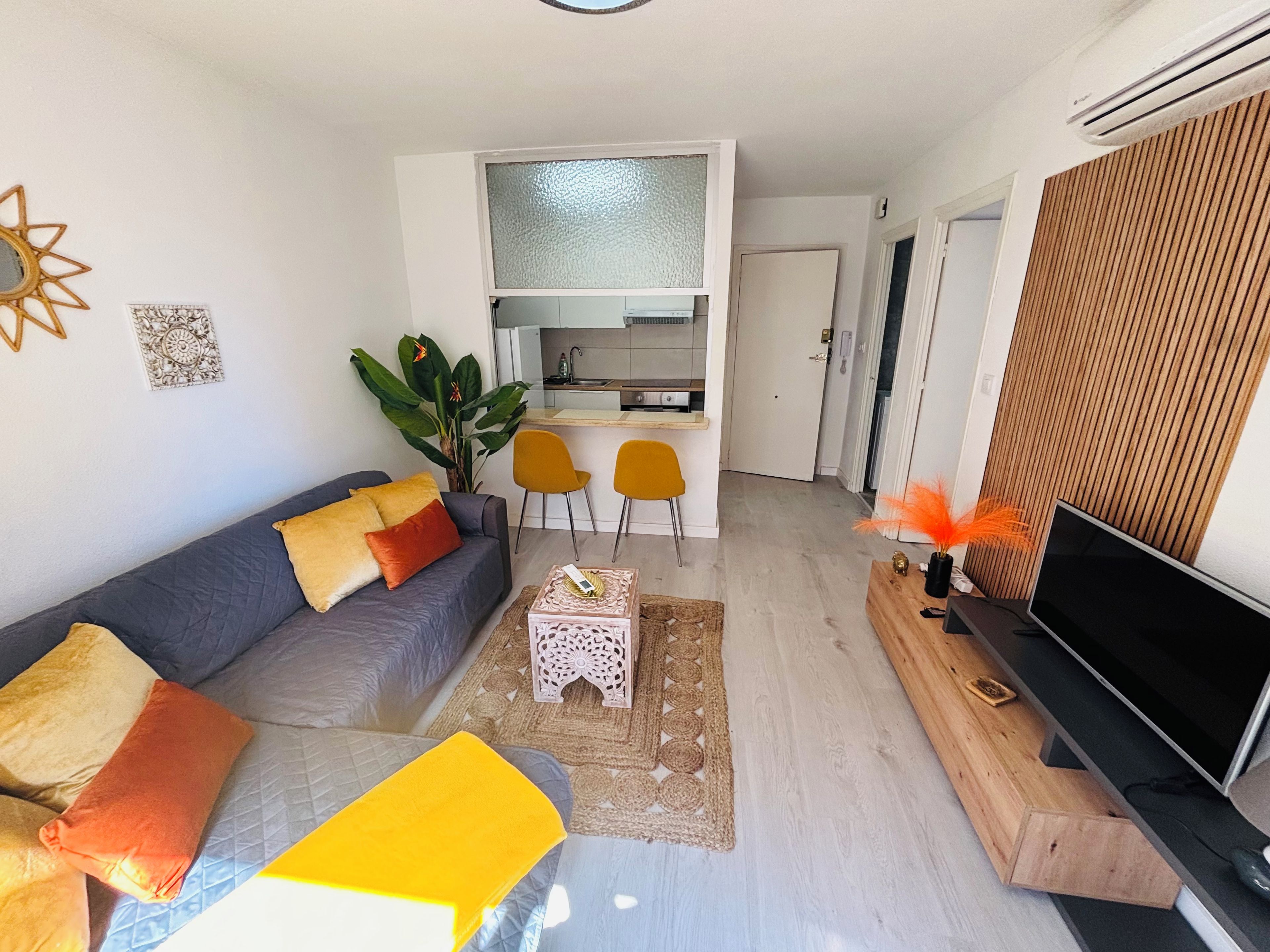 A modern living room with a sofa, coffee table, and a TV. There is a kitchen area with a dining table and chairs.