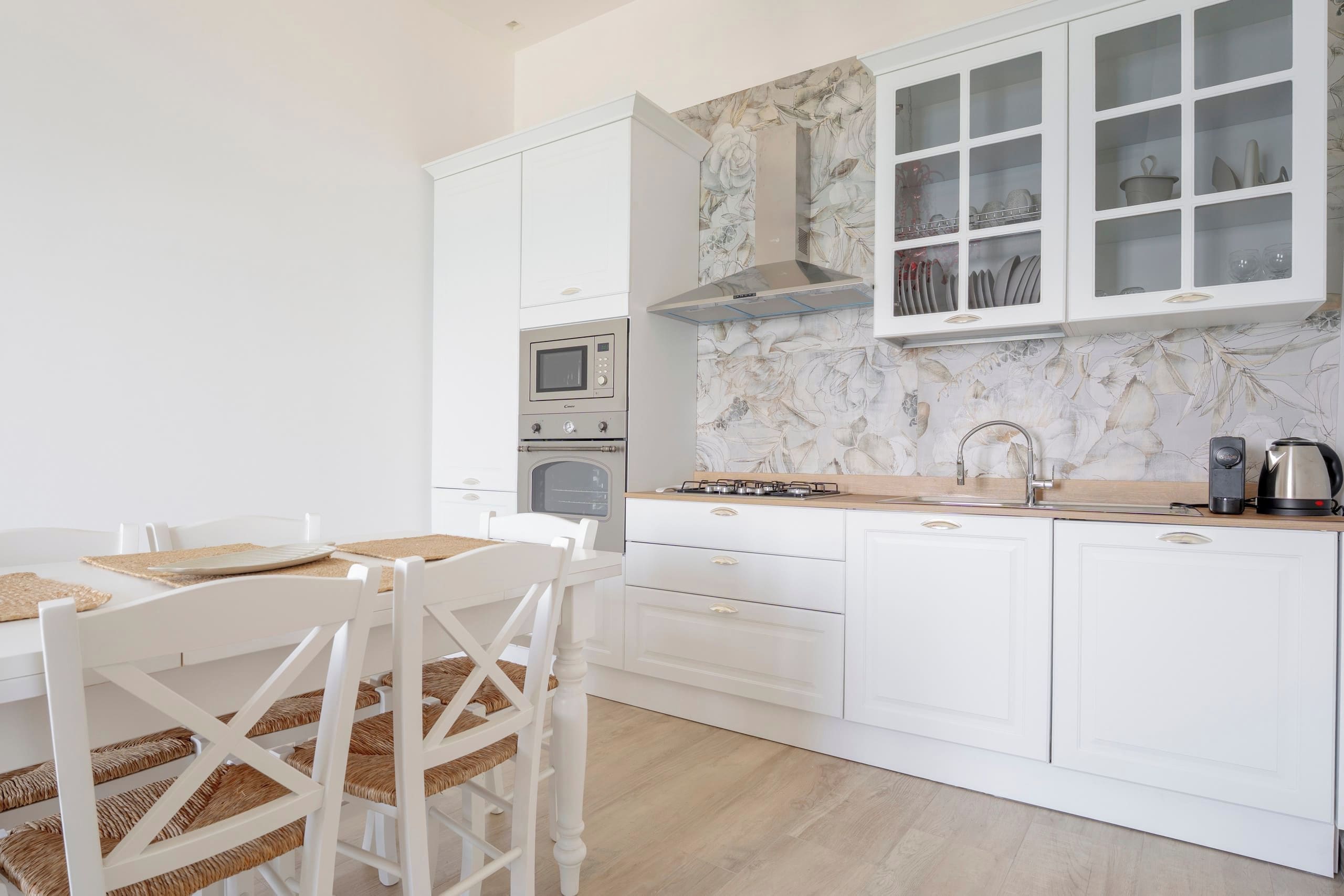 Une cuisine moderne avec des meubles blancs, un four encastré, un four à micro-ondes, une cuisinière à gaz et un évier.
