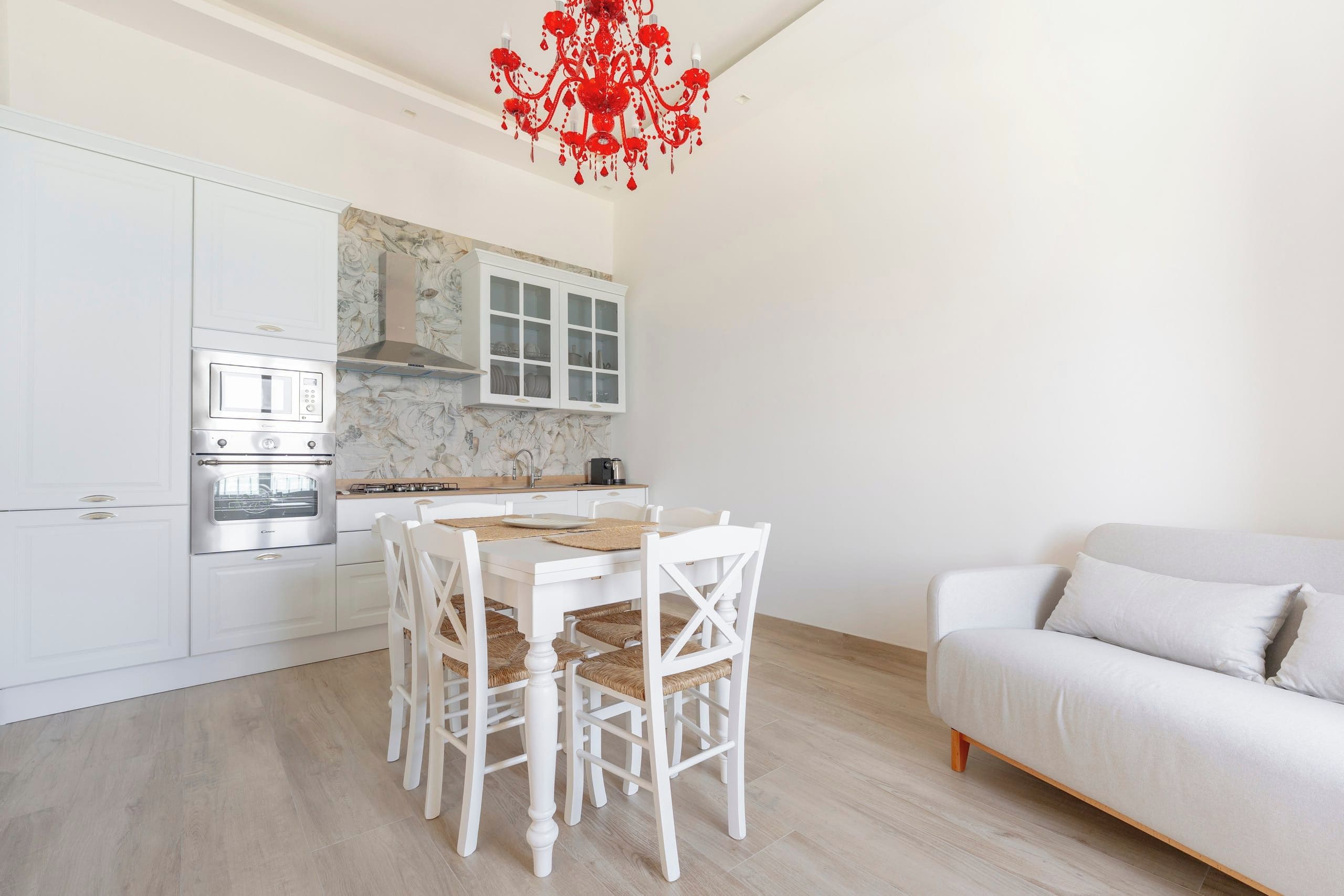 Une cuisine moderne avec des meubles blancs, une table à manger avec des chaises, et un canapé blanc dans le salon attenant.