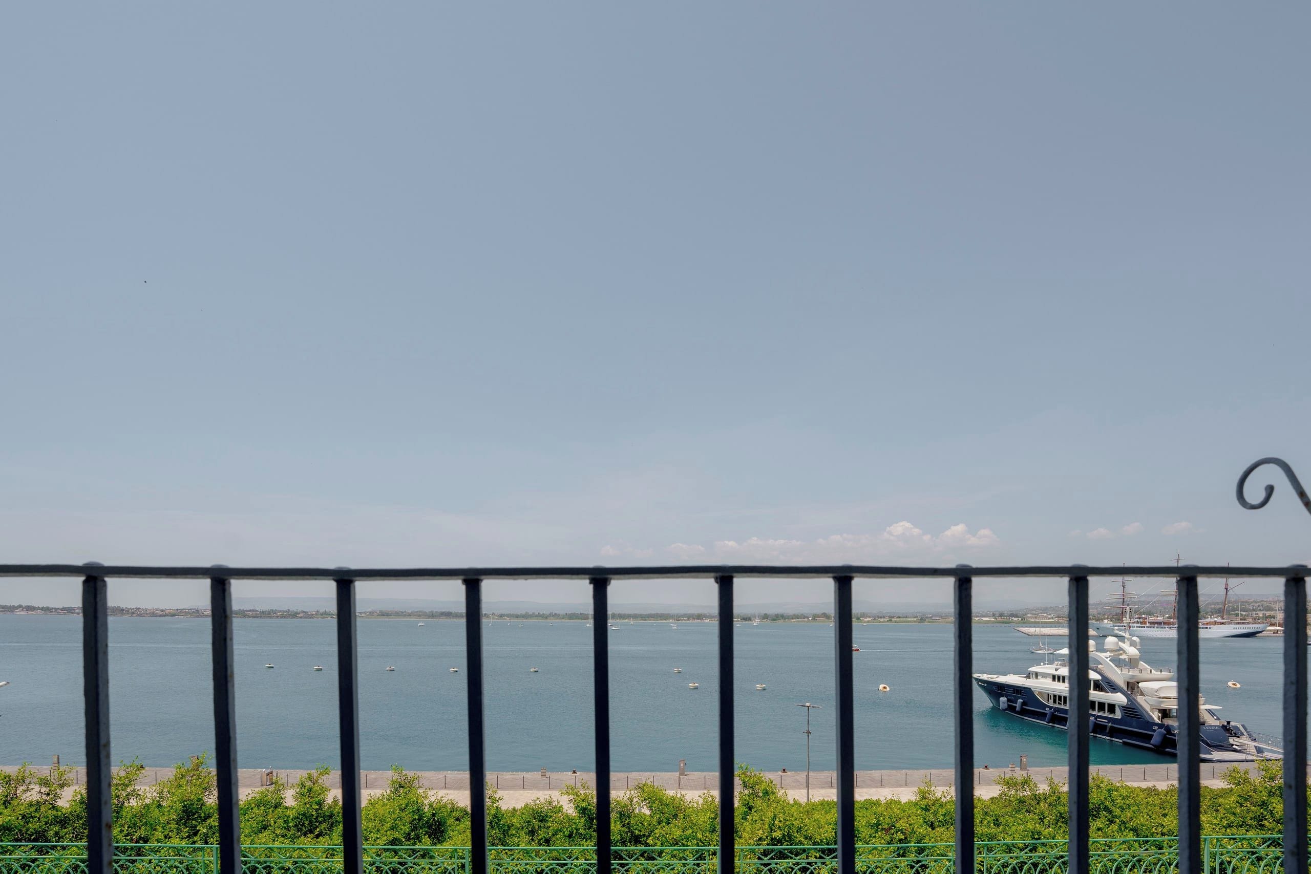 Une vue d’une marina où plusieurs bateaux sont amarrés, avec un ciel dégagé et une rambarde métallique au premier plan.