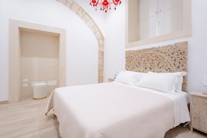 A bedroom with a bed, a nightstand, a decorative headboard, a mirror, and a door. - Ortigia Prestige (Siracusa)