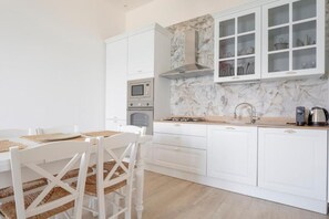 Una cocina moderna con armarios blancos, protector contra salpicaduras de mármol y un comedor con sillas y mesa blancos.