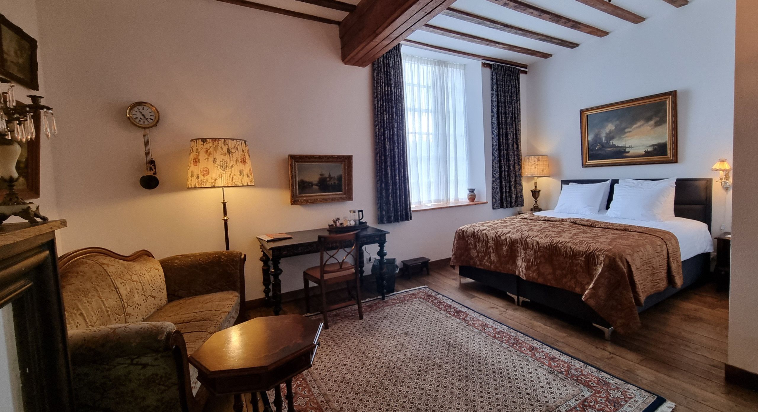 A traditional room with a bed, a desk, a chair, a lamp, a clock, and a painting.