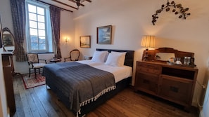 A hotel room with a bed, a wooden dresser, a chair, a desk, a lamp, and a window with curtains.