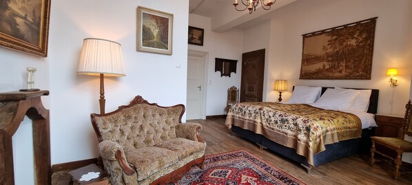 A traditional bedroom with a large bed, a classic armchair, and a wooden floor.