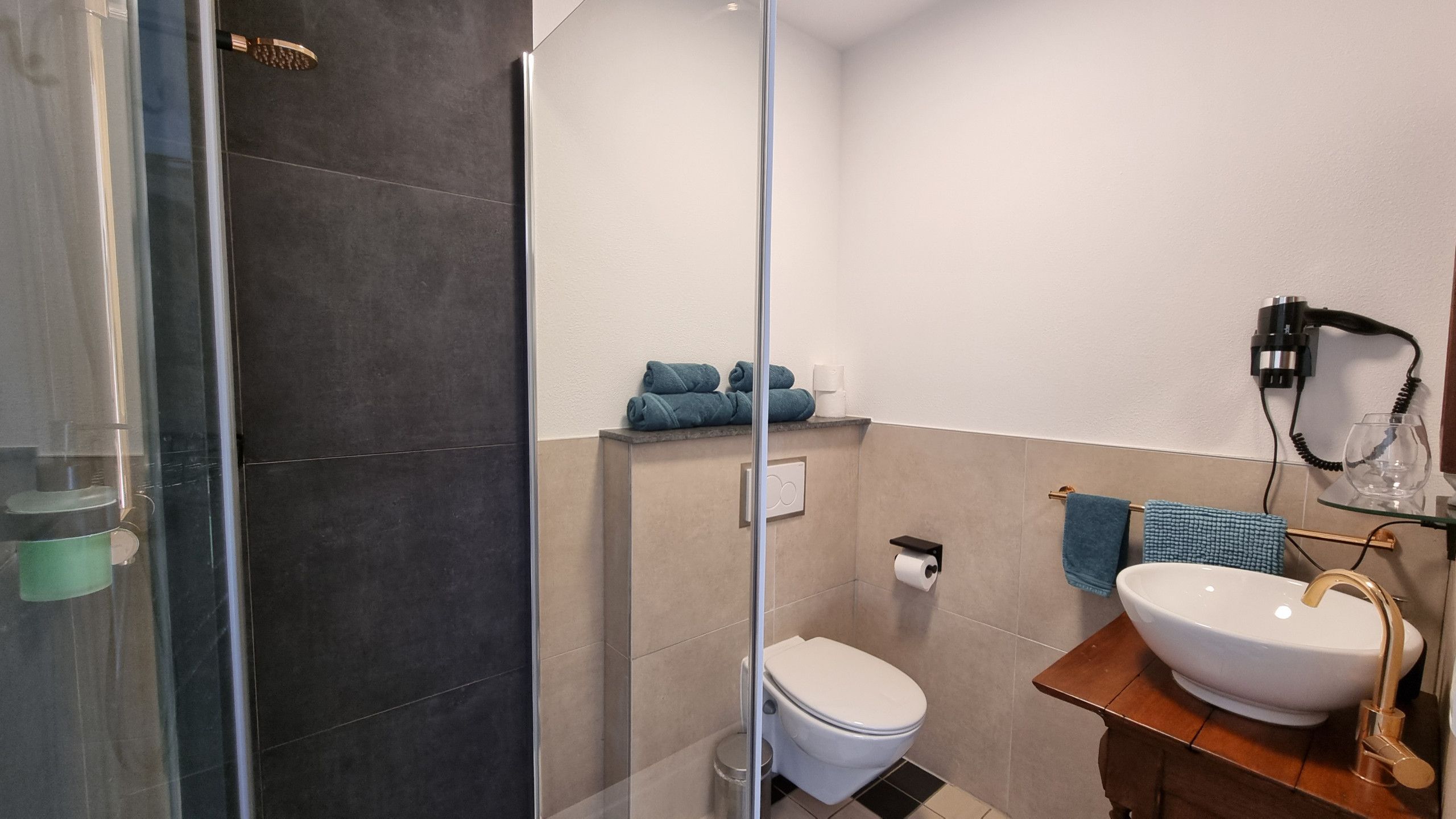 A bathroom with a glass shower enclosure, a toilet, a sink with a gold faucet, and a towel rack with blue towels.
