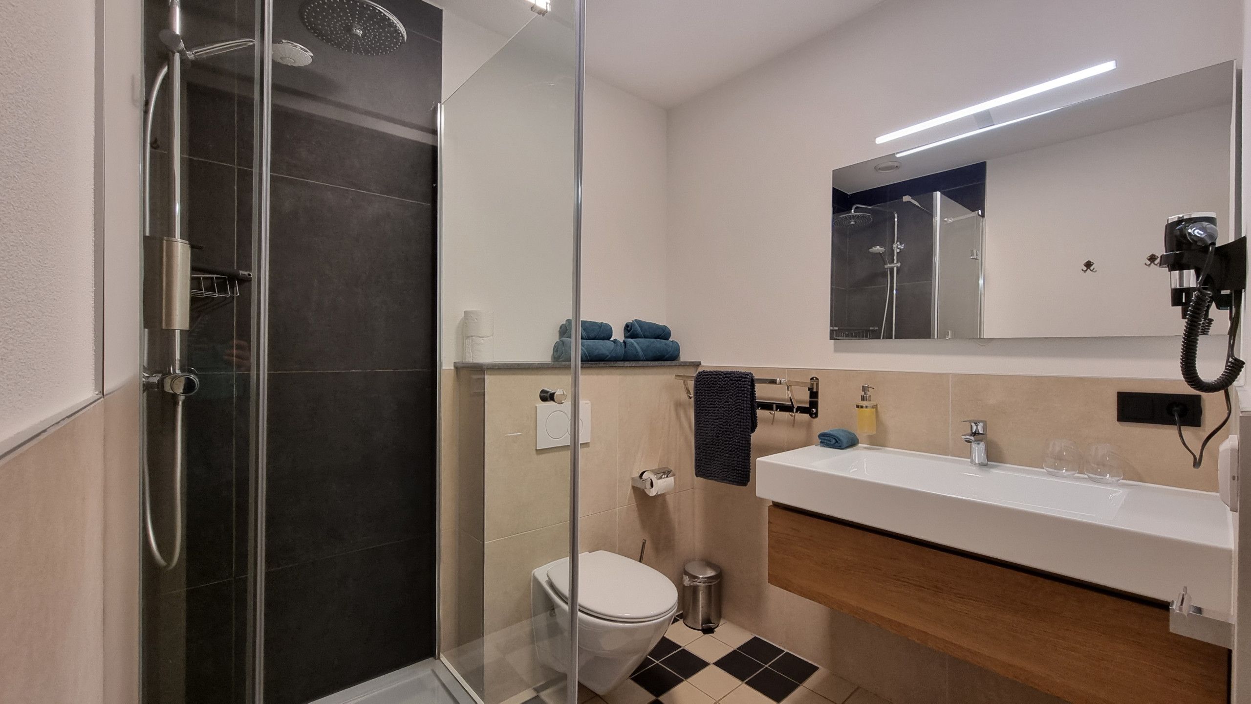 Une salle de bain moderne avec une douche à parois de verre, des toilettes, un lavabo avec un miroir au-dessus et un porte-serviettes.