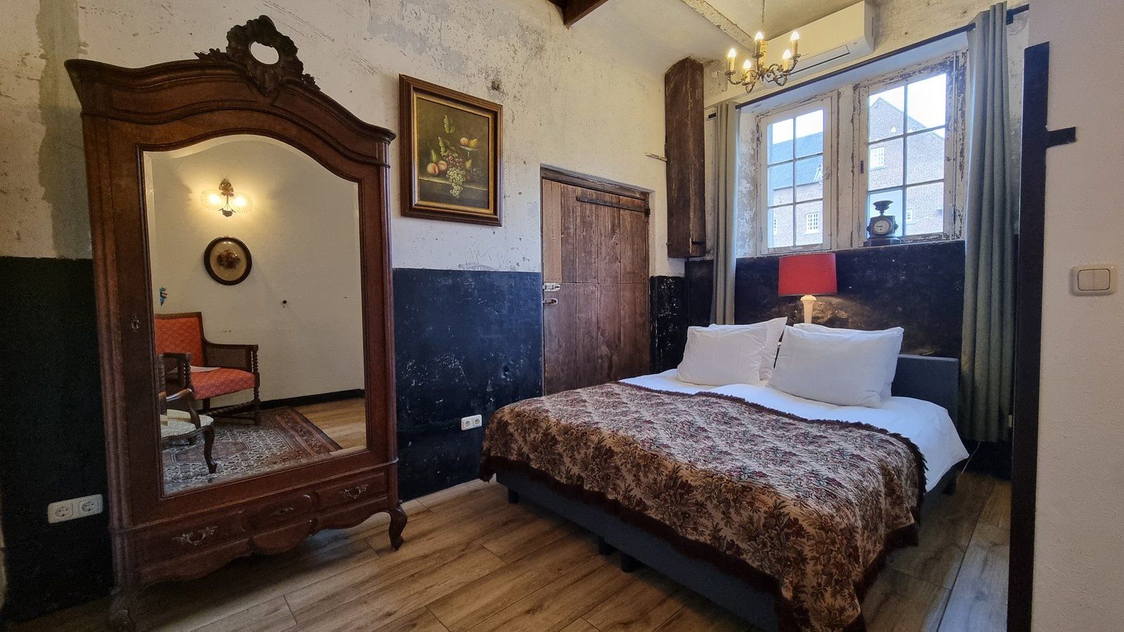 A bedroom with a large mirror, a bed with white linens, a wooden dresser, and a window with curtains.