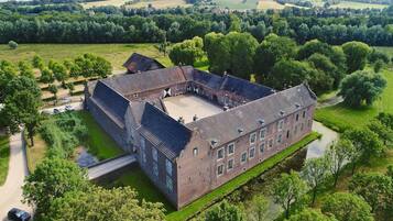 Een groot, historisch gebouw met een binnenplaats, omringd door weelderige begroeiing en velden.