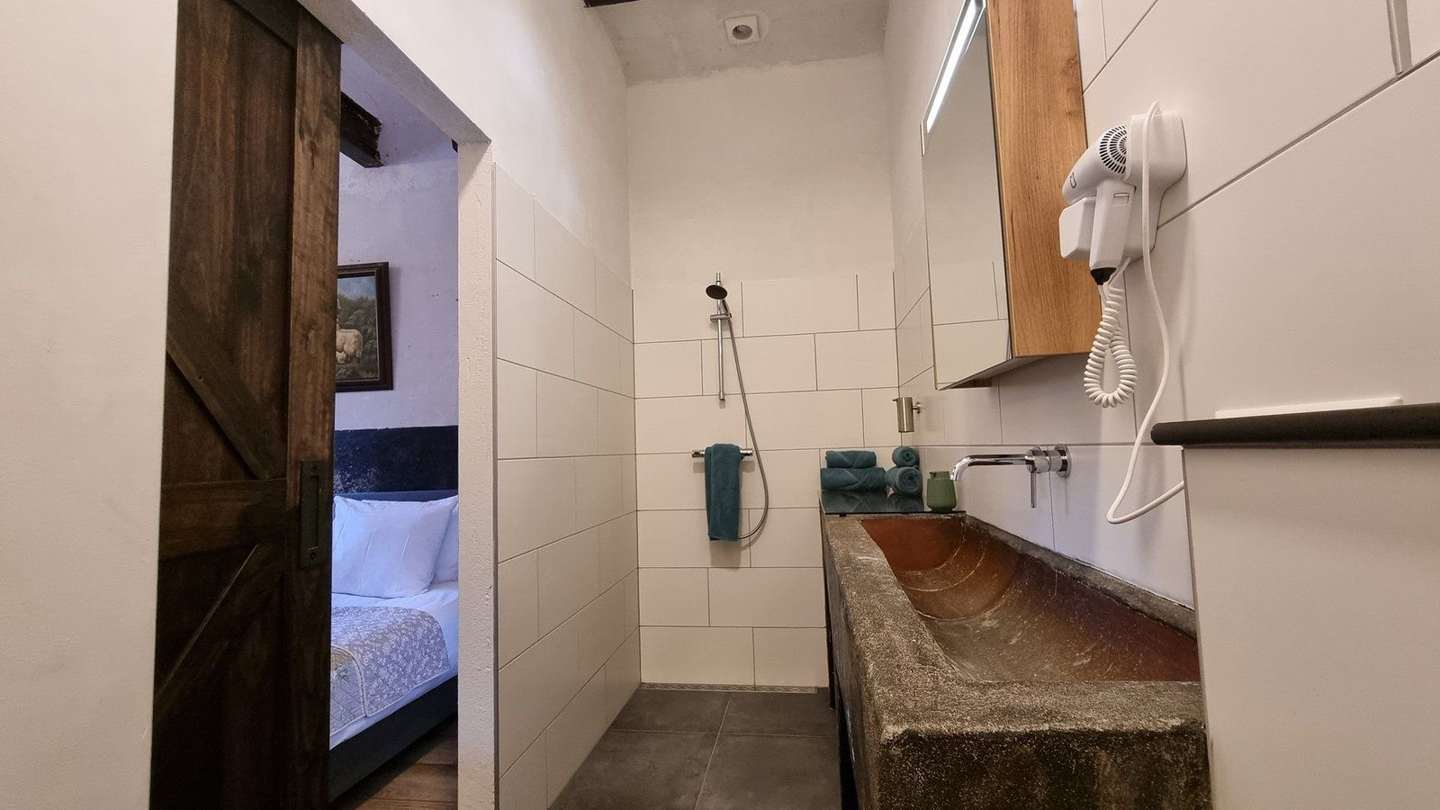 A bathroom with a shower, a sink with a stone countertop, a hairdryer, and a towel rack.