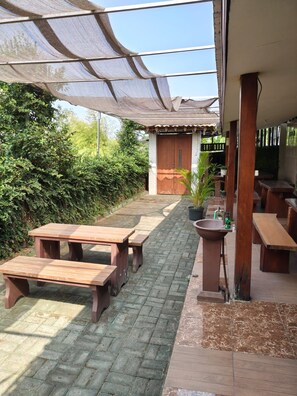 An outdoor patio area with wooden tables and benches, a sink, and a covered walkway. - Hotel O Banyu Asem Residence (Banyuwangi)