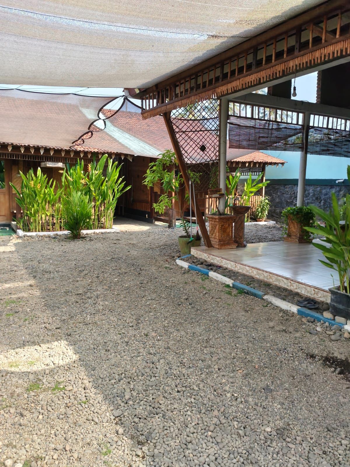 A covered outdoor area with a gravel floor, wooden structures, and potted plants.
