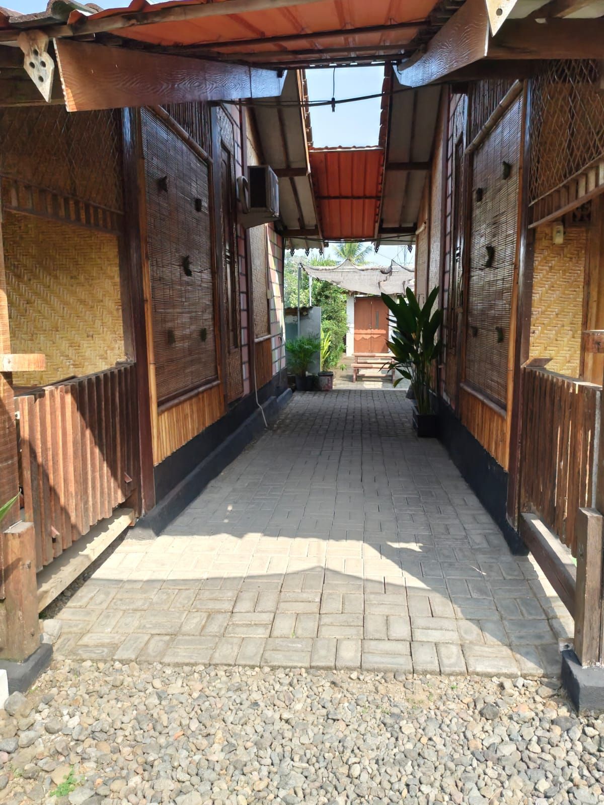 A covered walkway with wooden walls and a tiled floor, leading to a building with a sloped roof.