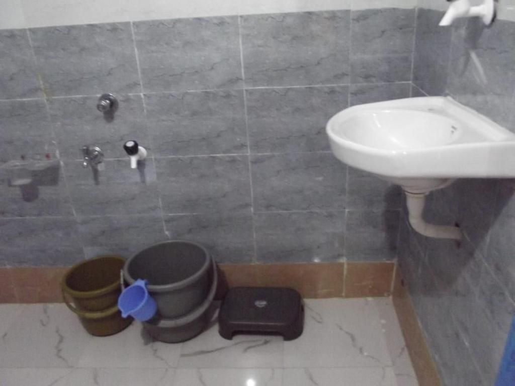 Un baño con lavamanos, ducha e inodoro. Hay cubetas y una balanza en el suelo.