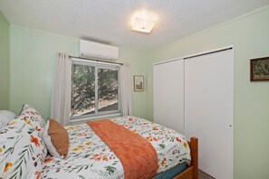 A bedroom with a bed, a window with blinds, an air conditioning unit, and a door. - Lake View Cabin Game Room (Crestline)