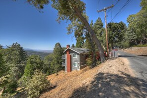 A two-story house with a red brick chimney, a balcony, and a view of the surrounding forest and hills. - Lake View Cabin Game Room (Crestline)