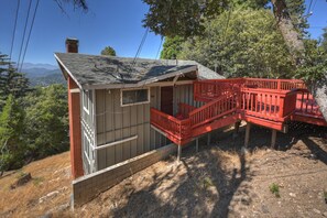 A small cabin with a red deck, surrounded by trees and a mountainous backdrop. - Lake View Cabin Game Room (Crestline)