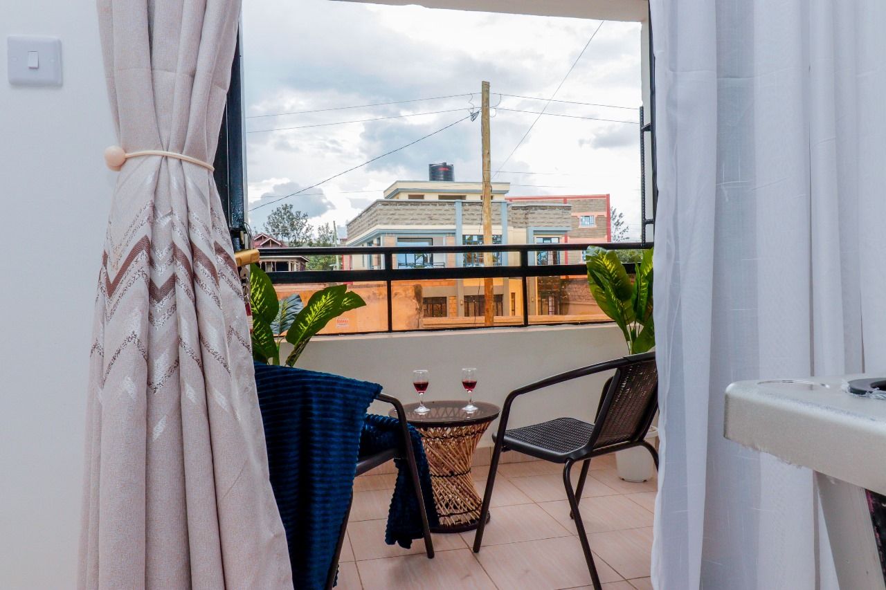 Un balcon avec une table et des chaises, deux verres de vin rouge et une vue sur les bâtiments en arrière-plan.