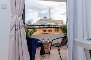 A balcony with a table and chairs, two glasses of red wine, and a view of buildings in the background. - Naivasha - Gateaway View Palace  (Naivasha)