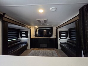 A compact RV interior with a central seating area, a television, and a kitchenette. - Russells River Retreat (Gadsden)