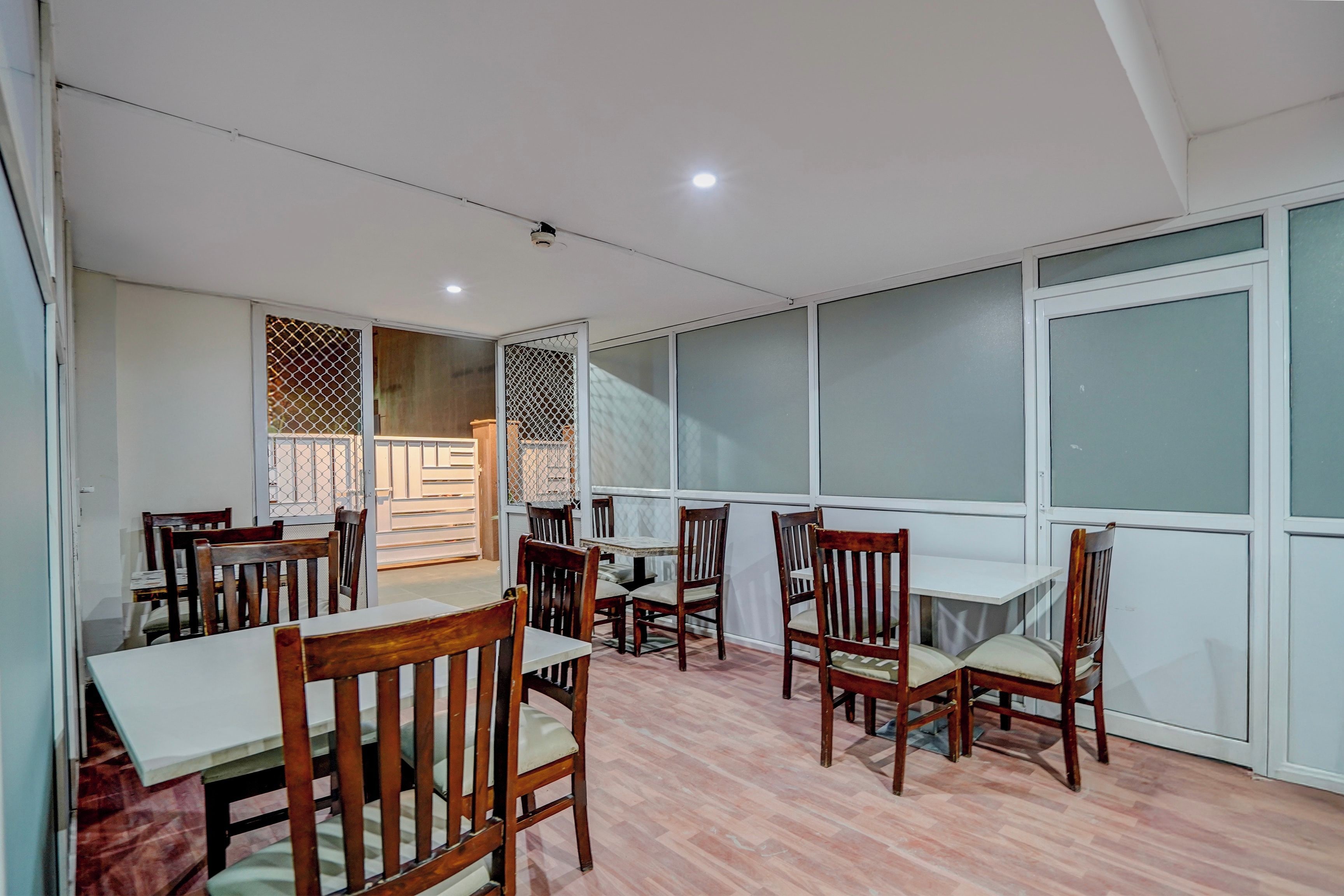 A dining area with wooden chairs and tables, a patterned wall, and large windows.