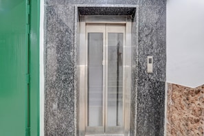 A marble elevator door with a glass panel, set within a building with a green door frame and a marble wall. - Townhouse DLF Phase-4 MG Road Cyber Hub (Gurugram)