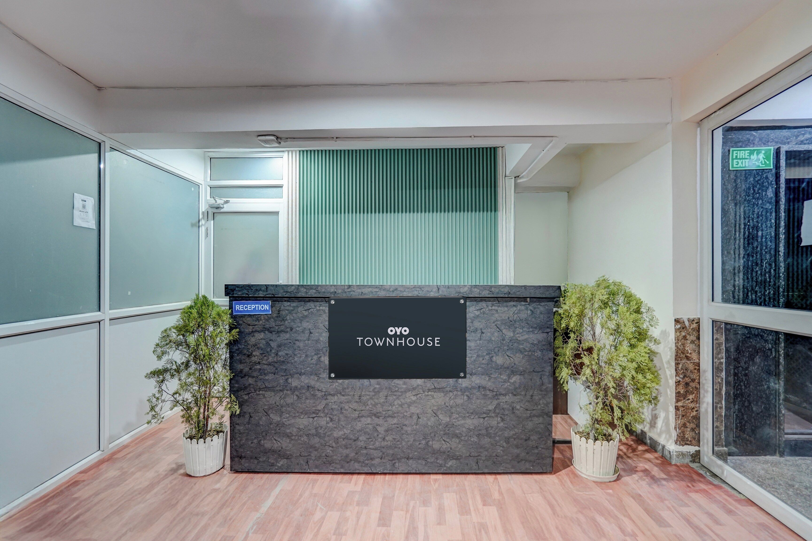 A reception desk with a sign reading 'OYO TOWNHOUSE' in a modern interior with wooden flooring and potted plants.