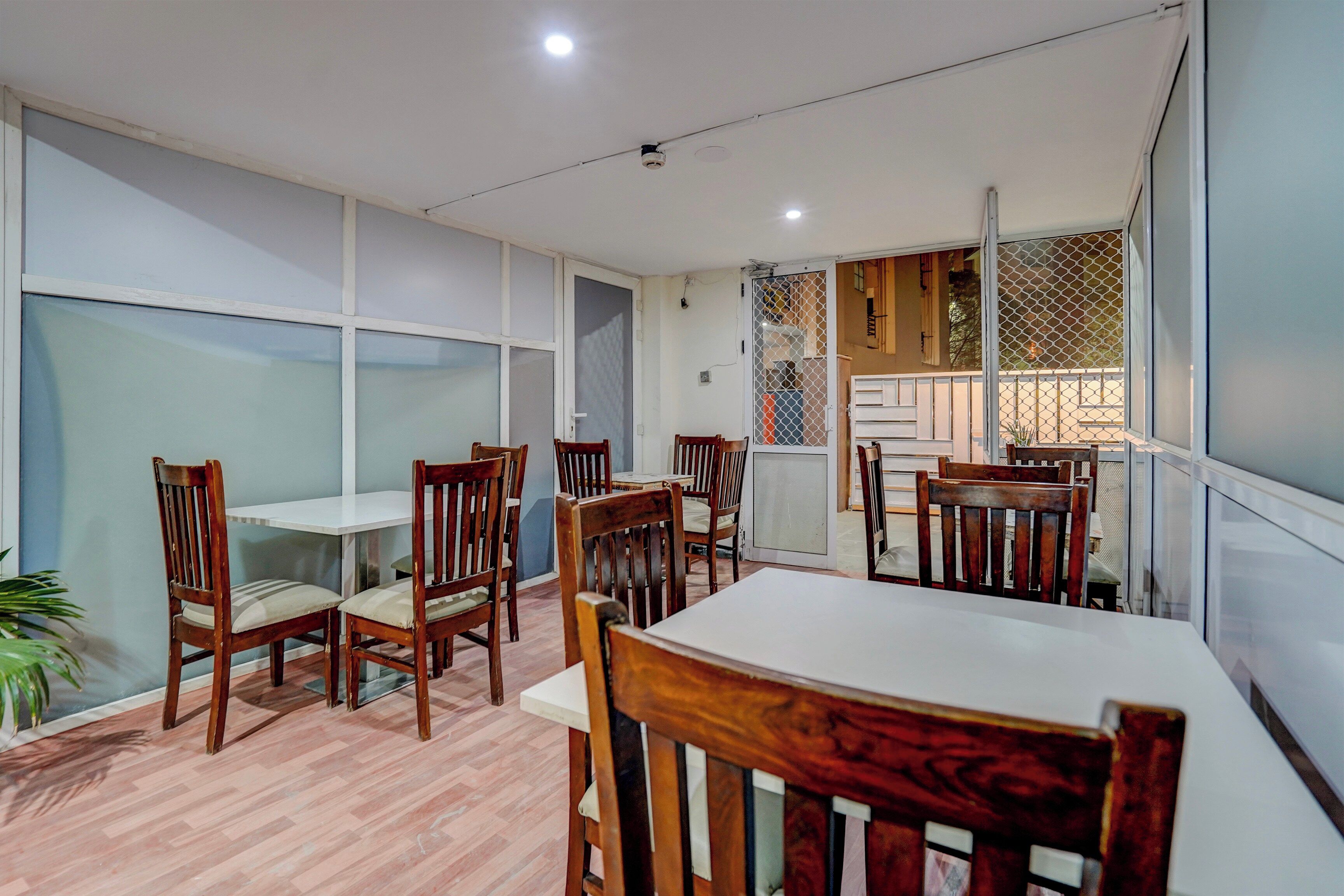 A dining area with wooden tables and chairs, a white ceiling, and a view through a window with a decorative screen.