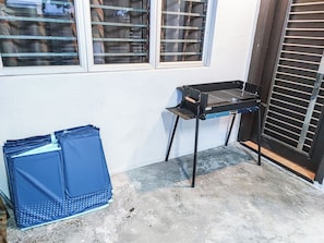 Un pequeño espacio al aire libre con una mesa de parrilla metálica y un contenedor azul contra una pared.