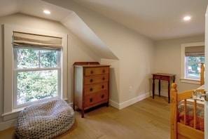 A room with a sloped ceiling, a wooden dresser, a small table, a bean bag chair, and a crib. - Wooded Retreat w/ Porch & Fire Pit in Stone Ridge (Stone Ridge)