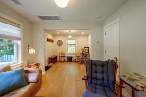 A spacious living room with a wooden floor, a large armchair, a sofa, and a dining area with a table and chairs. - Wooded Retreat w/ Porch & Fire Pit in Stone Ridge (Stone Ridge)