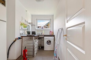 A compact laundry room with a washing machine, a sink, a drying rack, and a fire extinguisher. - Charming Bro Retreat, Luxury Comfort & Modern Amenities (Bro)