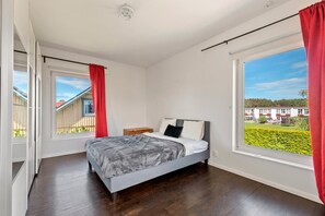A bedroom with a bed, a nightstand, and a window with a view of a residential area.