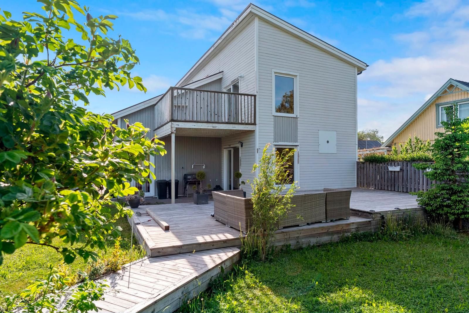 Une maison à deux étages avec un balcon, une terrasse et un petit jardin.