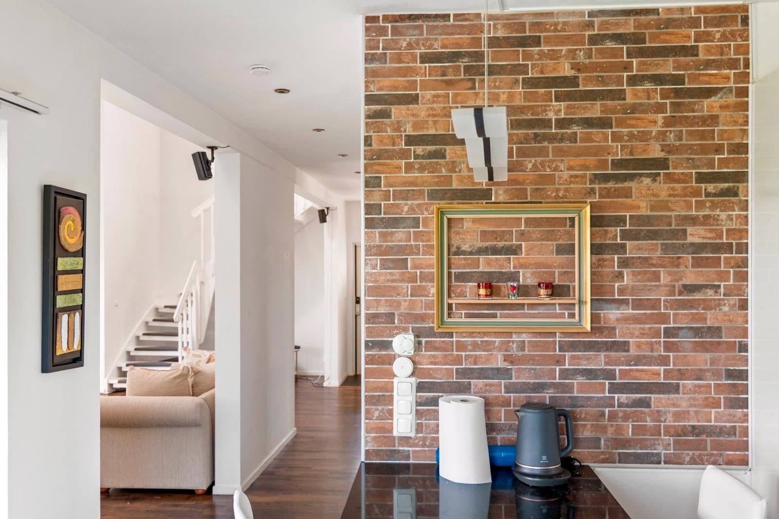 A modern kitchen with a brick wall, a coffee machine, and a framed picture on the wall.