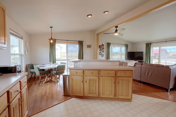 A modern kitchen with wooden cabinets, a dining area with chairs, a large island, and a view of the outdoors through the windows. - Walkable Fairplay Home w/ Mtn Views! (Fairplay)