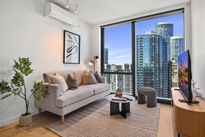 Ein modernes Wohnzimmer mit einem grauen Sofa, einem Couchtisch, einer Topfpflanze und einem großen Fenster mit Blick auf die Stadt.
