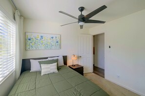 A bedroom with a bed, a ceiling fan, a nightstand with a lamp, a door, and a window with blinds. - Private Pool Oasis: Modern 3BR/2BA, Sleeps 8 (San Diego)