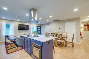 A modern kitchen with a central island, built-in oven, and dining area with wooden chairs. - Williamsburg Home for Colonial & Theme Park Trips (Williamsburg)