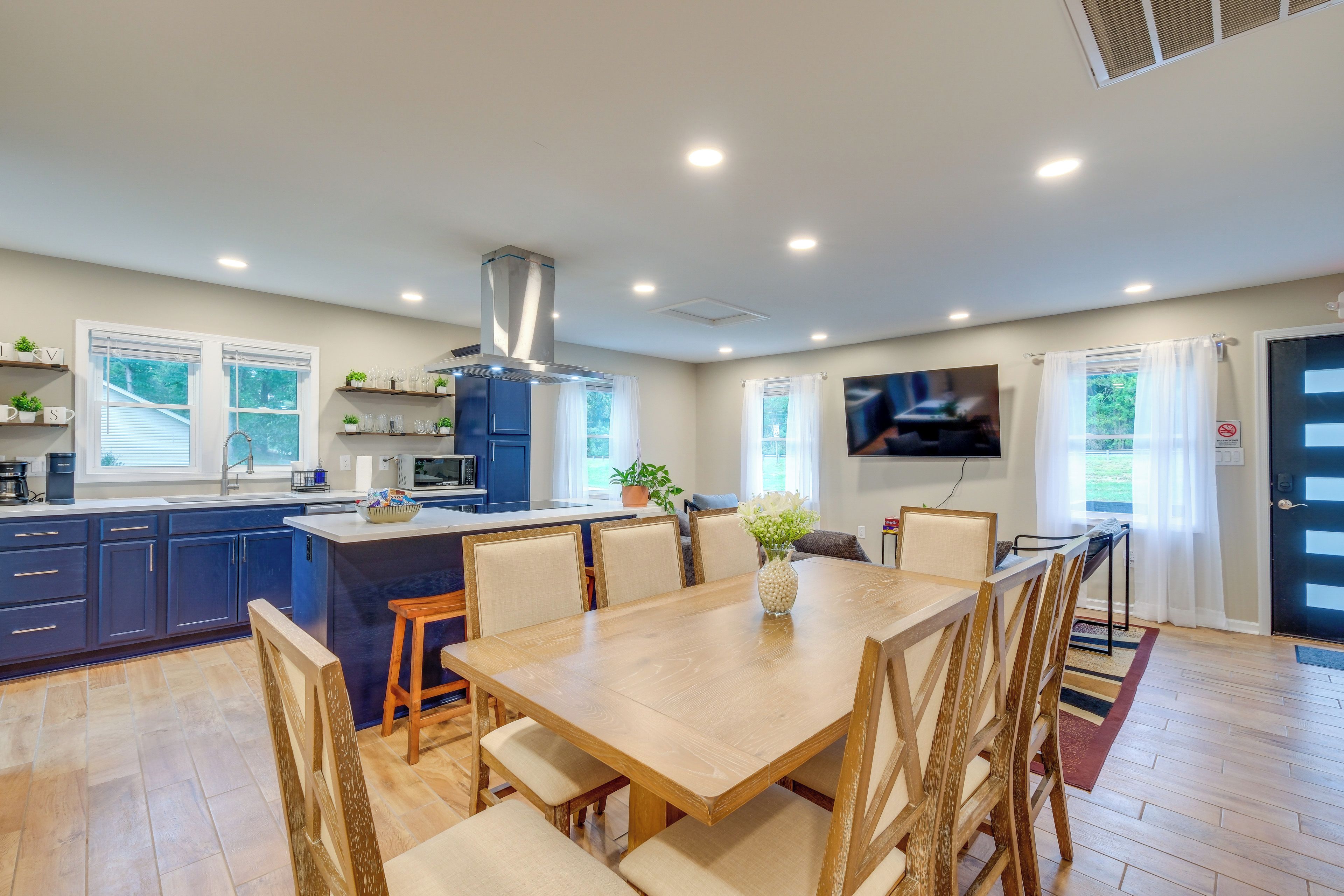 Une cuisine moderne avec des meubles de couleur bleu foncé, un îlot central et un coin repas comprenant une table et des chaises en bois.