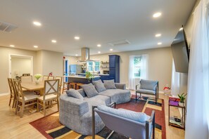 A modern living room with a sectional sofa, a dining table with chairs, a kitchen area, and a large window with curtains. - Williamsburg Home for Colonial & Theme Park Trips (Williamsburg)