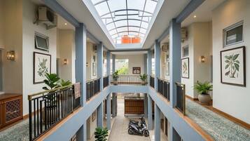 A multi-level atrium with a glass ceiling, potted plants, and a scooter parked in the center.