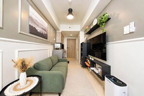 A modern living room with a green sofa, a flat-screen TV, and a small table with a vase. - Cozy 1-bedroom Suite with Balcony near MOA Pasay City (Pasay City)