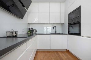 Functional kitchenette with white cabinetry, dark worktops, built-in appliances. - Warsaw | Obrzeżna 1B | Bright Apartment | Desk (Warszawa)