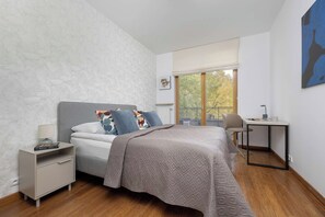 A bedroom with a bed, bedside table, lamp, and a view of the outdoors through a window. - Warsaw | Obrzeżna 1B | Bright Apartment | Desk (Warszawa)