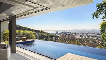 Une piscine extérieure moderne avec vue sur la ville, une terrasse en bois et un espace détente.