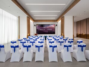 A conference room with rows of white chairs with blue sashes, a large screen, and a podium. - Elong Hotel Shenzhen Pingshan (Shenzhen)
