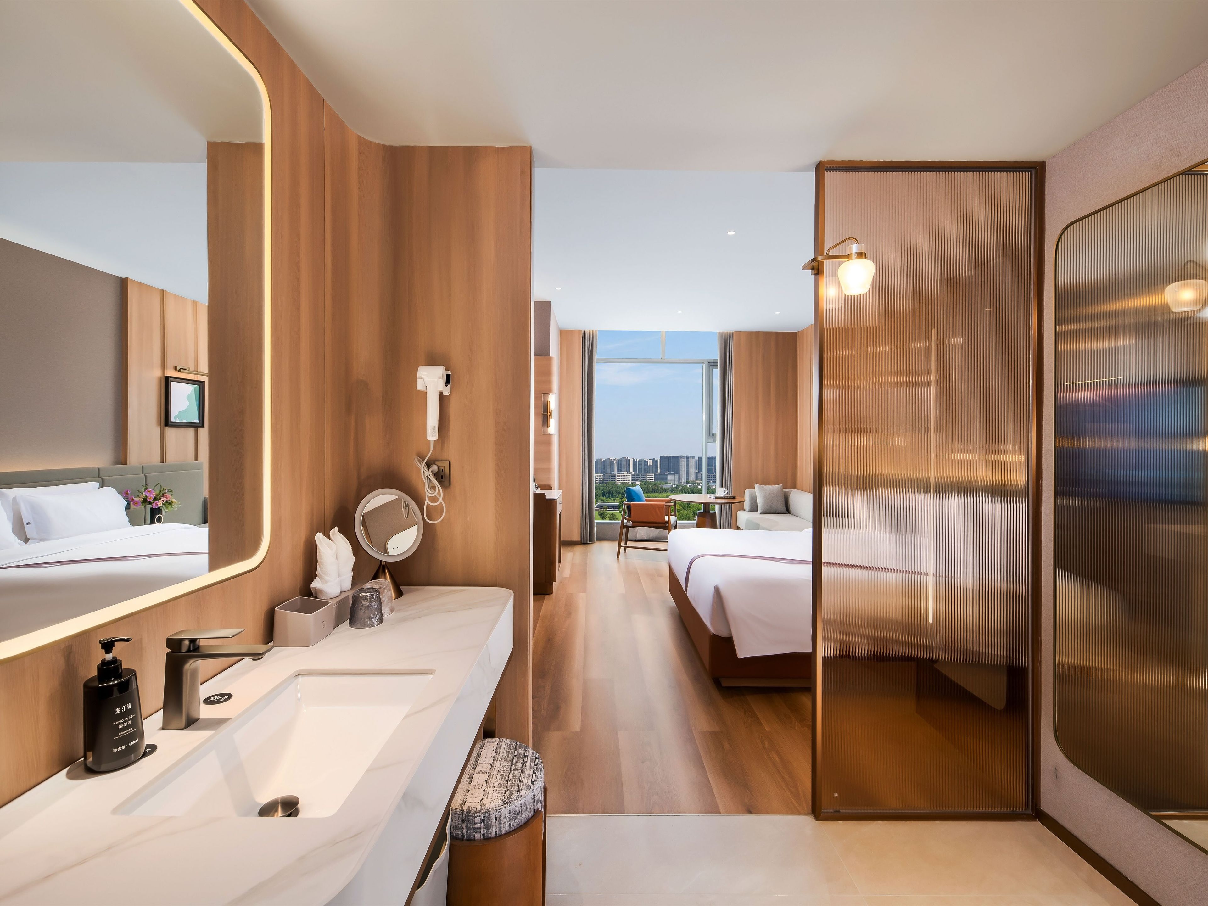 Habitación de hotel moderna con un espejo grande, una tocador con lavamanos y una cama con vistas a la ciudad.