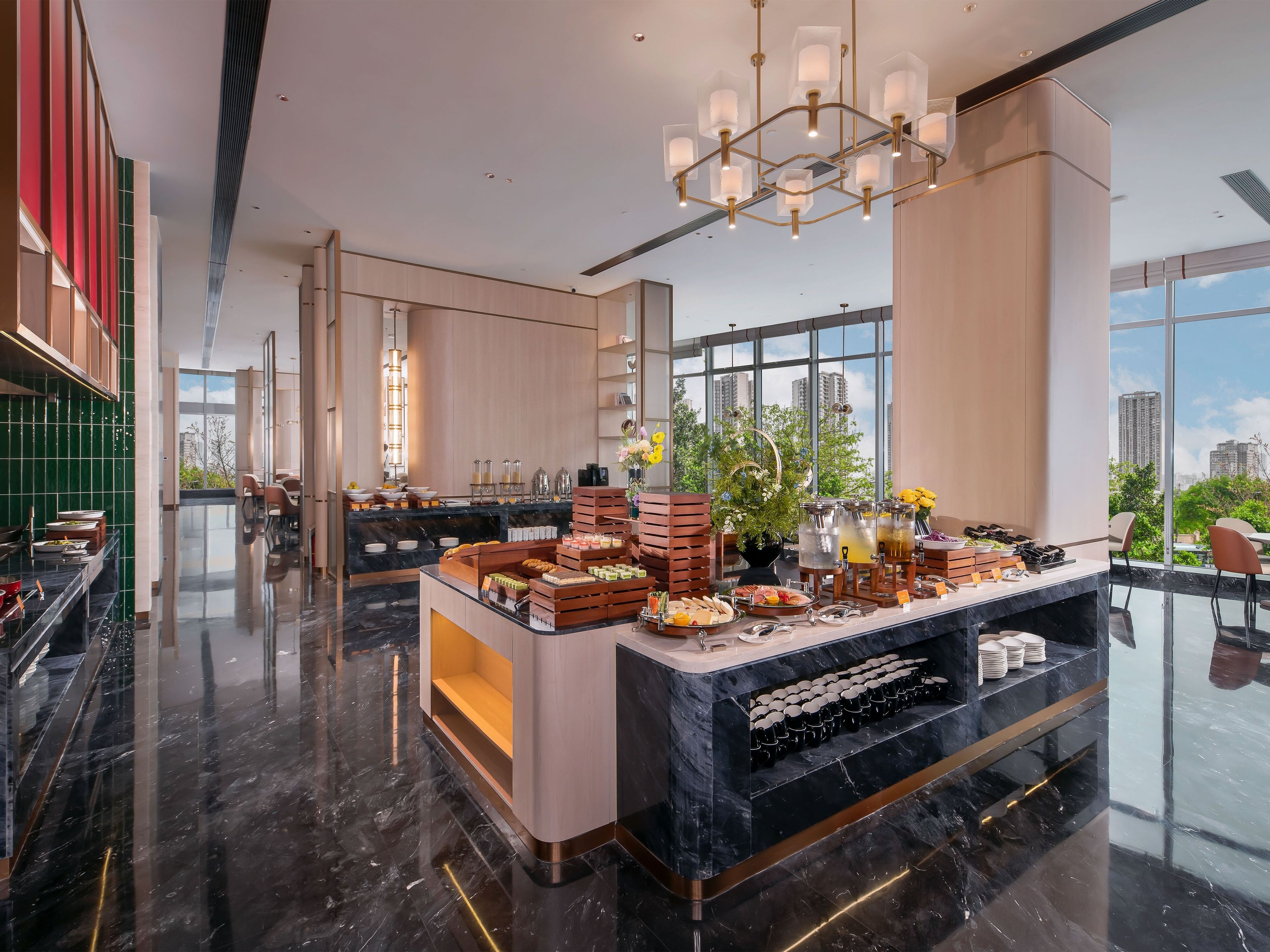 A modern hotel lobby with a marble floor, a central buffet area, and large windows offering a city view.